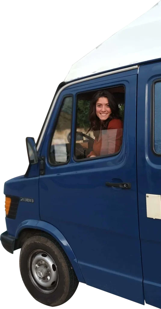 Coach Joy Lumi looking out of the driver side window of her blue Mercedes 208D camper van.